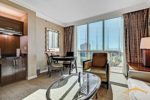 A hotel room with a dining table, chairs, a sofa, a glass table, a kitchen area, and large windows with curtains. - MGM Signature (Las Vegas)