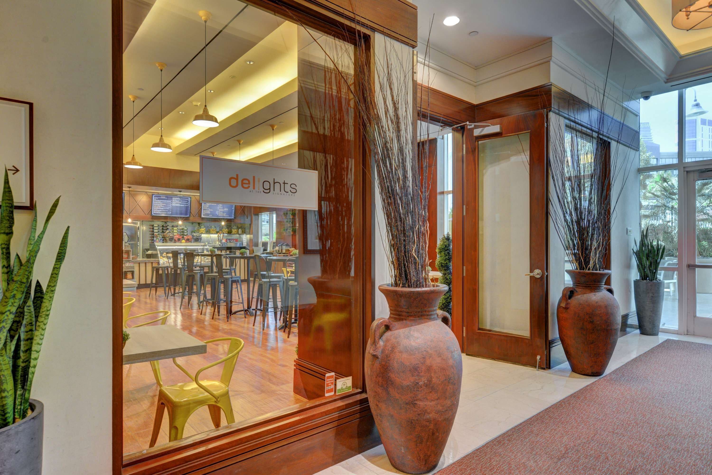 A modern interior with a reception area, large vases, and a dining space visible through the glass doors.