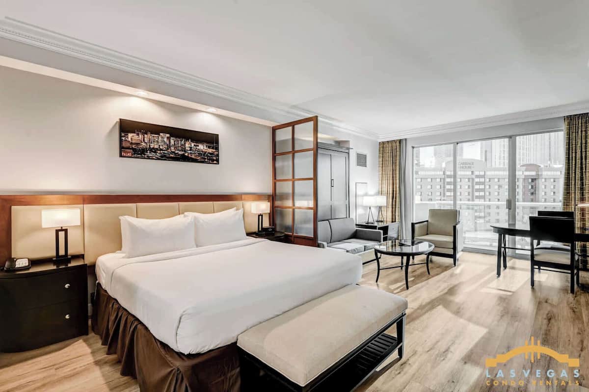 Habitación de hotel con una cama grande, un escritorio, una silla y vistas a la ciudad.