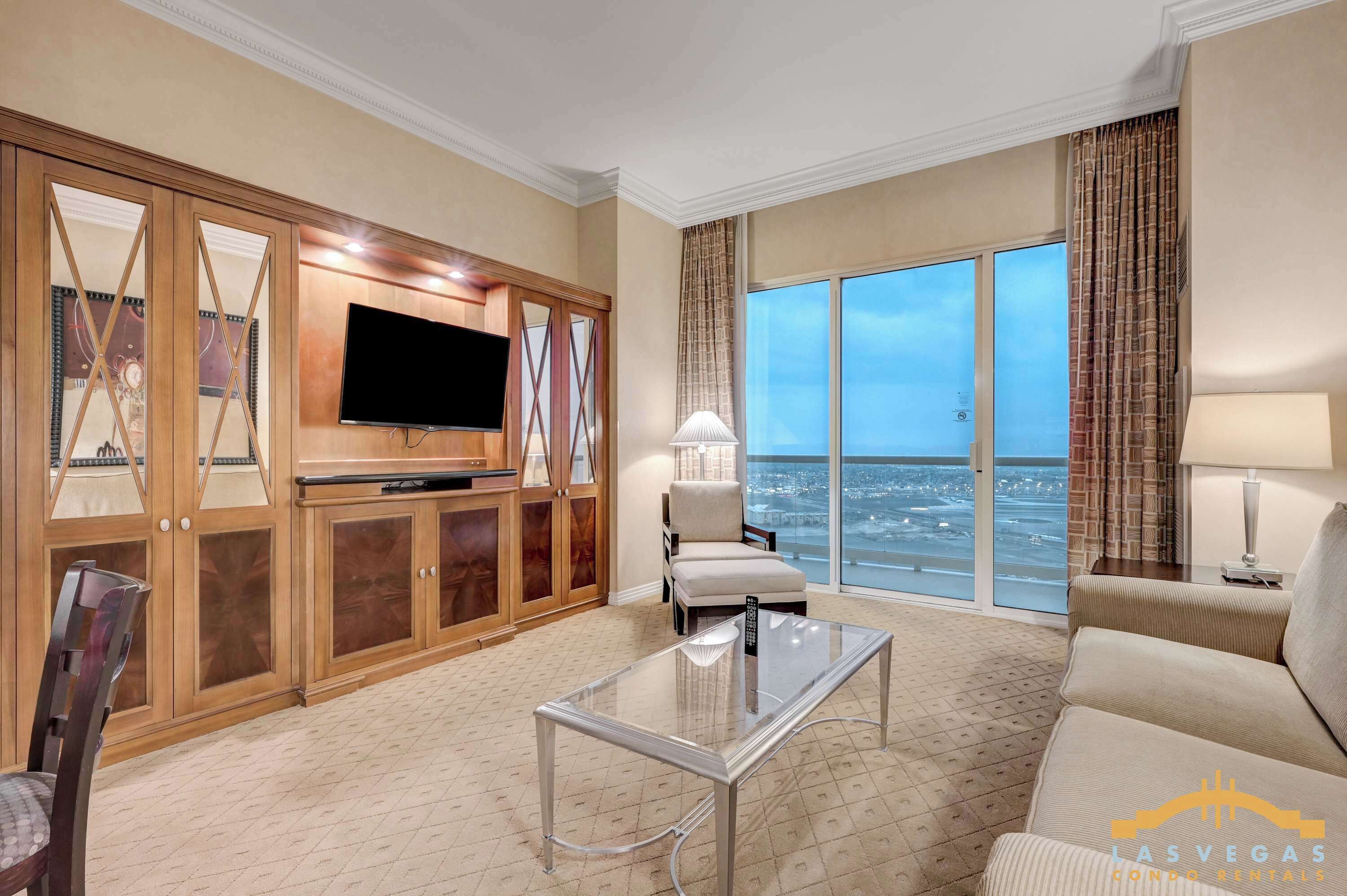 A hotel living room with a large TV, a glass coffee table, a sofa, and a view of the ocean.