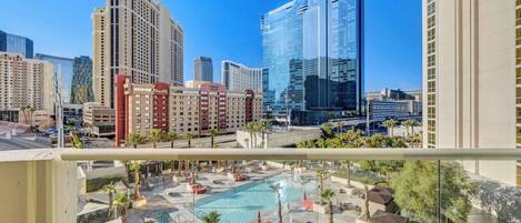 Un hotel con zona de piscina, varios edificios altos al fondo y un cielo azul despejado.