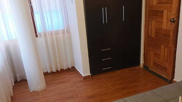A bedroom with a bed, a wooden wardrobe, a window with curtains, and a radiator. - Apartment in Barrio de San Blas (Cusco)