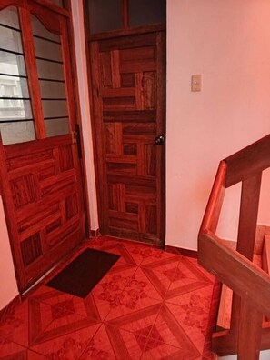 Eine Holztür mit einem geometrischen Muster, eine schwarze Fußmatte und eine Holztreppe.