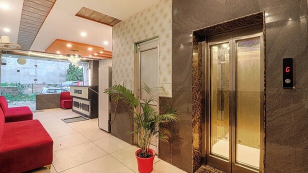 Een hotel lobby met een receptiebalie, rode zitplaatsen, een kamerplant en een lift.