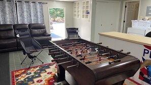 Una habitación con mesa de fútbol, sofá, alfombra estampada y ventana con cortinas.