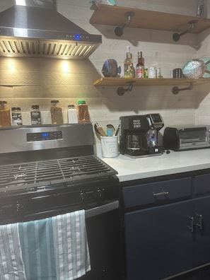 A kitchen with a stove, a coffee maker, and various spices on the counter.