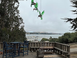 A wooden deck with a table and chairs, overlooking a marina with boats and a distant view of hills. - Harbor Heron Natural Setting With Bayview, Wildlife Abounds and Room for Boats (Bodega Bay)