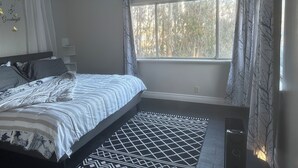 Un dormitorio con cama, ventana con cortinas, alfombra estampada y un adorno en la pared.
