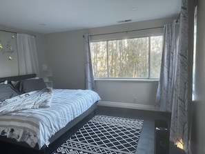 A bedroom with a bed, a window with curtains, a patterned rug, and a wall with a decorative item. - Harbor Heron Natural Setting With Bayview, Wildlife Abounds and Room for Boats (Bodega Bay)