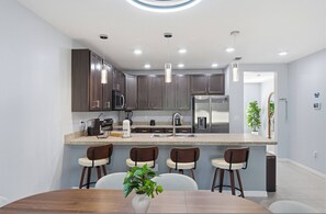 A modern kitchen with dark wood cabinets, stainless steel appliances, and a central island with bar stools. - 3BR Family Home at Fiesta Key Near Parks (Kissimmee)