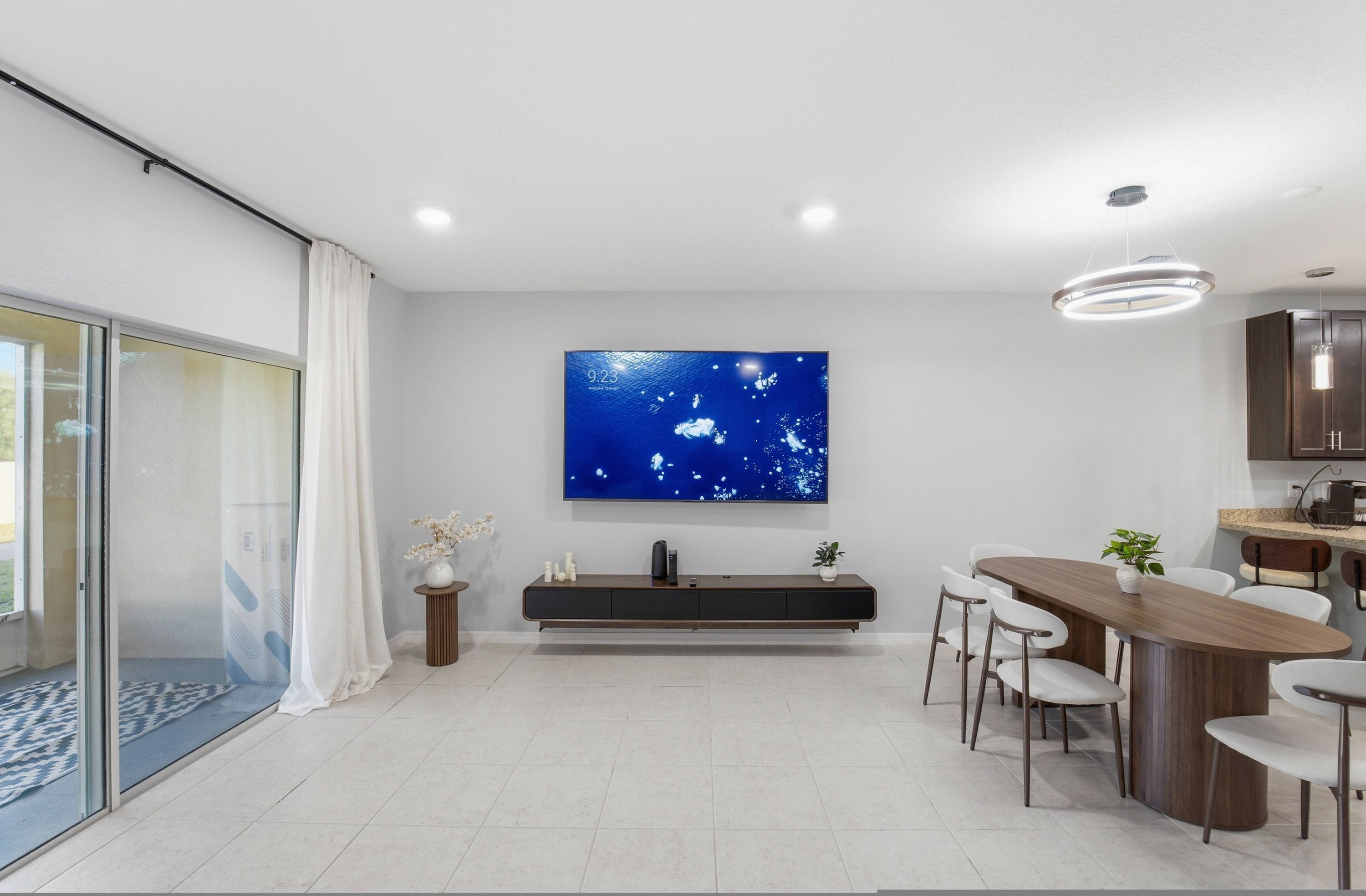Una cucina moderna con un ampio televisore a schermo piatto, un'area pranzo con tavolo e sedie in legno, e una porta scorrevole in vetro che dà su un balcone.