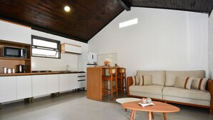 Eine moderne Küche mit weißen Schränken, einer Mikrowelle und einer Kaffeemaschine. Im Wohnbereich befindet sich ein Holzessttisch mit Stühlen und ein beiges Sofa.