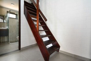 A wooden staircase in a modern interior with a white brick wall and a glass shower area. - Casa na Praia dos Ingleses -NIN019 (Florianópolis)