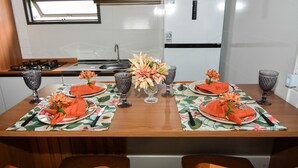 Ein Esstisch ist mit Tellern, Servietten und einer Blumenvase in einer Küche mit Kühlschrank und Fenster gedeckt.
