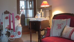 A room with a red sofa, a table with a lamp, and a mirror reflecting a window. - Guest Room "Les Charmilles - Beige Room" (Charny-sur-Meuse)