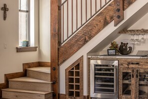Una escalera con escalones de madera y barandillas de metal, una cocina con nevera para vinos y una ventana con planta.