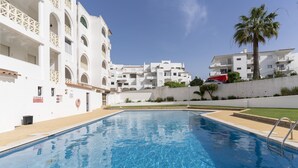A swimming pool with a clear blue water surface, surrounded by white buildings with balconies and a palm tree. - #376 Cozy Relaxing Getaway | Peaceful (Albufeira)