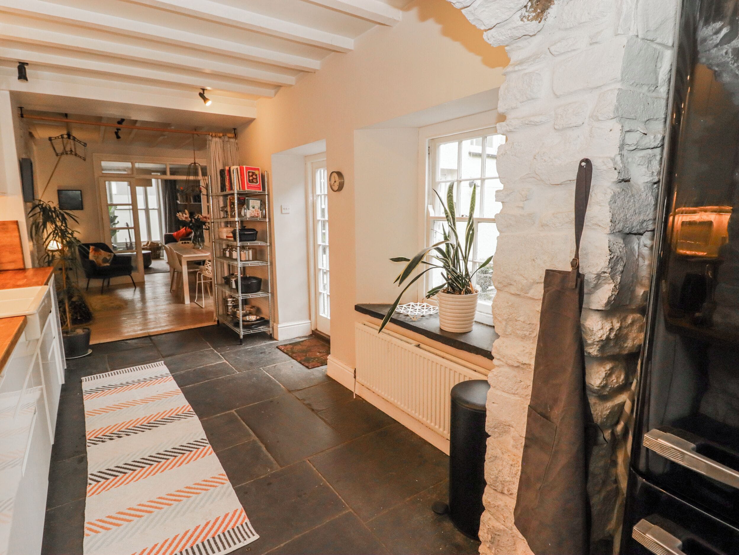 Una cocina con pared de piedra, un radiador, una planta en maceta y un cubo de basura negro.