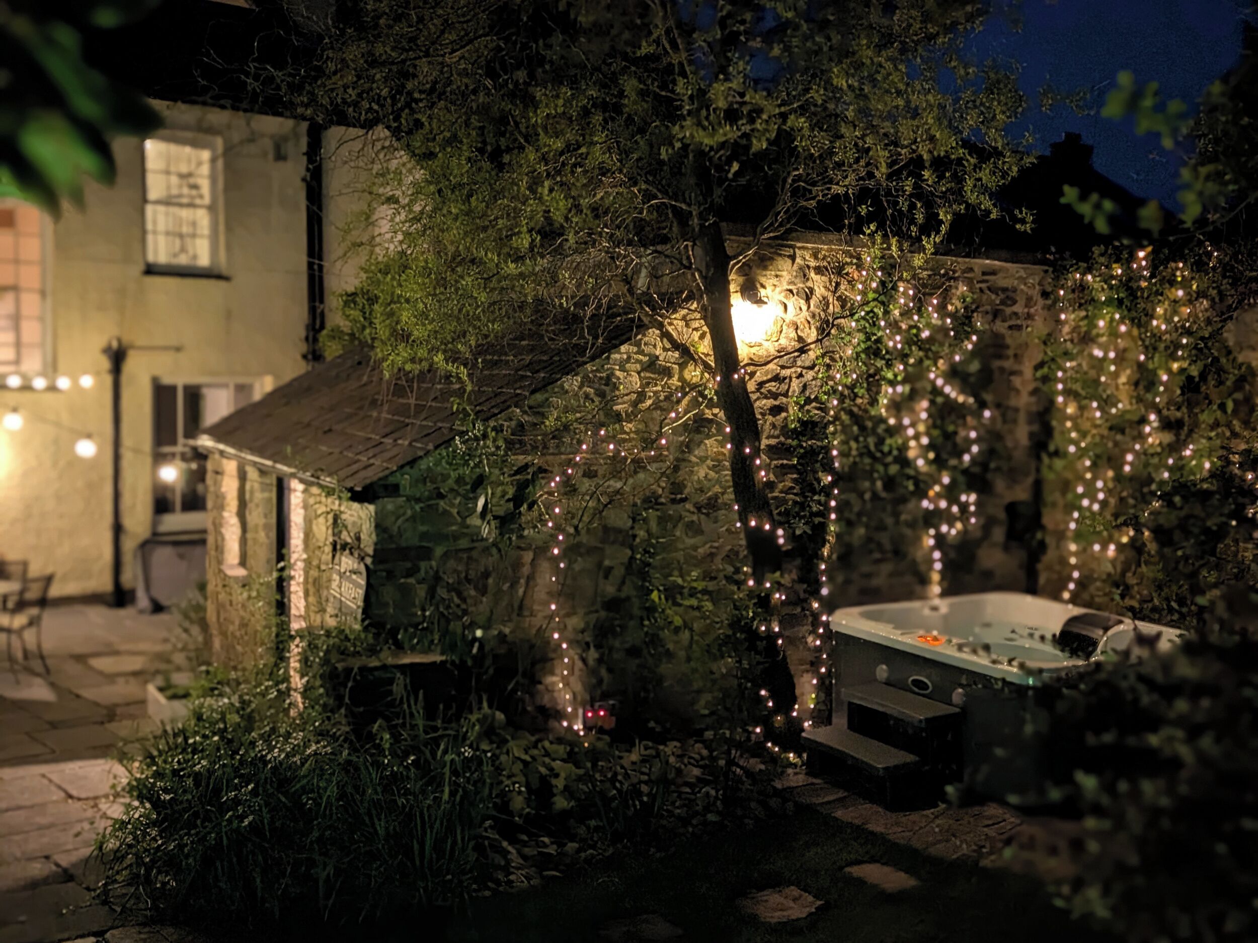 A stone building with ivy, a hot tub, and string lights.