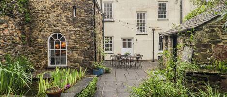 A stone building with a tiled patio, a small table with chairs, and a window with a view.