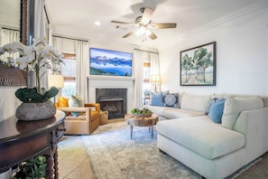 A living room with a fireplace, a sofa, a coffee table, a television, and a ceiling fan. - The Afton, 3BR Townhome by Velvet Ditch Villas (Oxford)