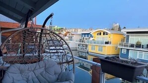 A balcony with a hanging chair, a view of colorful buildings, and a clear sky.