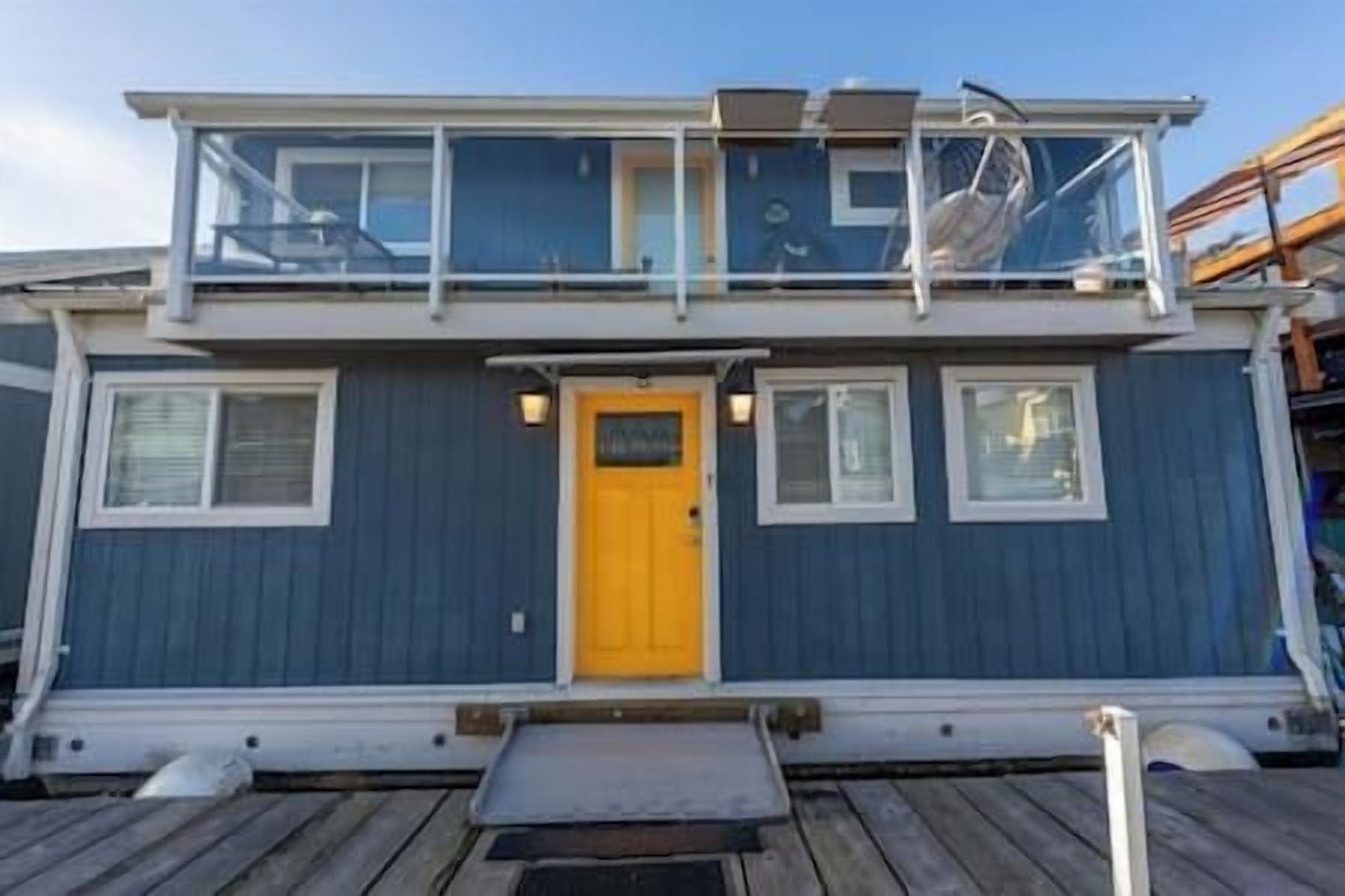 A two-story boat with a yellow door, windows, and a small deck area.