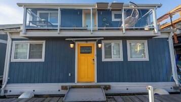 A two-story boat with a yellow door, windows, and a small deck area.