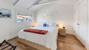 A bedroom with a bed, a nightstand, a window with a view, and a door.