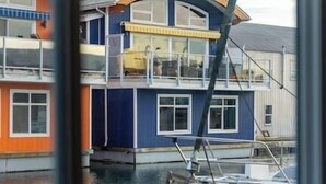 A multi-story houseboat with a balcony, a dock, and a boat in the foreground.