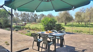 An outdoor patio with a table and chairs under a green umbrella, surrounded by a garden and trees. - Podere 23 - Two Bedroom Apartment, Sleeps 5 (Alghero)