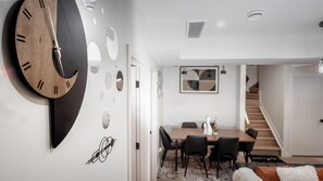 A modern interior with a wooden clock, abstract wall art, a dining area with chairs and a table, and a staircase. - Luxury Comfort Stay in Keswick | 2Bedrooms- 1Bath (Edmonton)