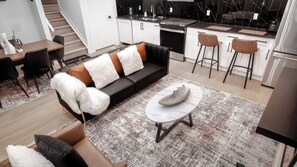 A modern kitchen with a black countertop, stainless steel appliances, and a dining area with a sofa and chairs. - Luxury Comfort Stay in Keswick | 2Bedrooms- 1Bath (Edmonton)