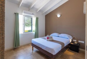 Un dormitorio con cama, mesita de noche, ventana con cortinas y un equipo de aire acondicionado.