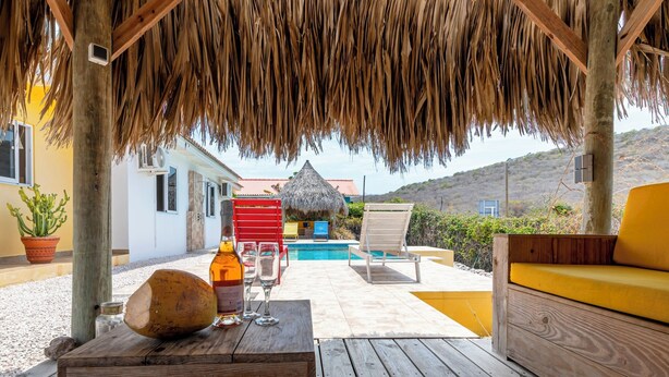 Une terrasse en bois surmontée d’un toit de chaume, une piscine et des sièges d’extérieur.