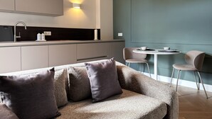 Une cuisine moderne équipée d’une cuisinière intégrée, d’un évier et d’un plan de travail sur lequel se trouve une machine à café. On y trouve également un coin repas avec une table ronde et deux chaises.