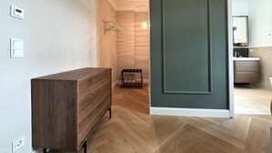 Une pièce comprenant une commode en bois, un porte-manteau et une porte donnant sur une salle de bain avec un miroir et un lavabo.
