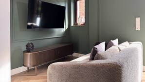 Un salon avec un téléviseur à écran plat fixé au mur, une console en bois et un canapé gris.