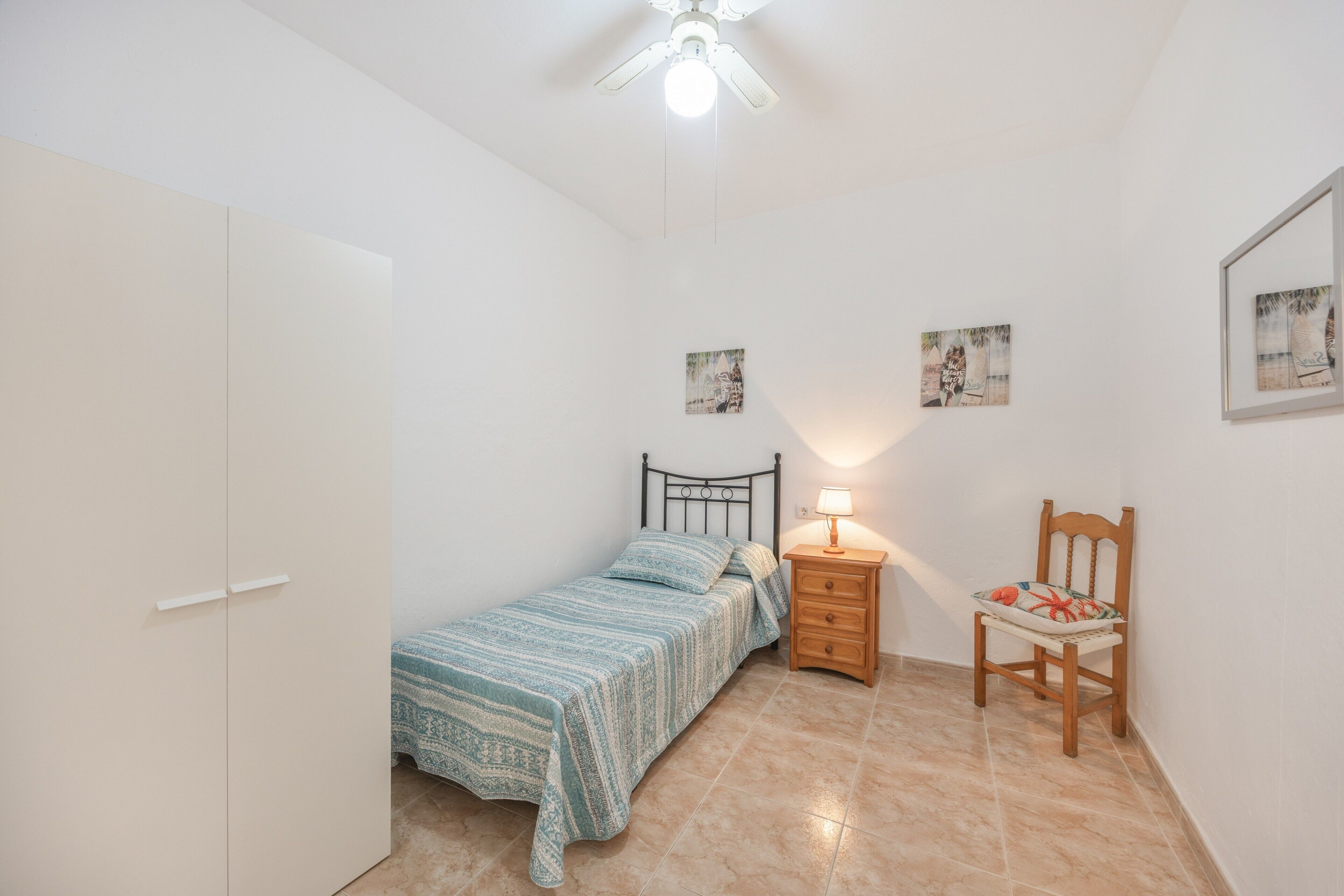 Un dormitorio con una cama, una mesita de noche, una silla y un ventilador de techo.