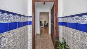 Un pasillo con baldosas estampadas, una puerta de madera y vista a una habitación con escritorio y silla.