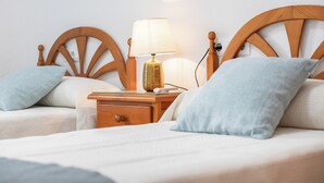 Un dormitorio con dos camas, cabeceros de madera, una mesita de noche con lámpara y un cajón.