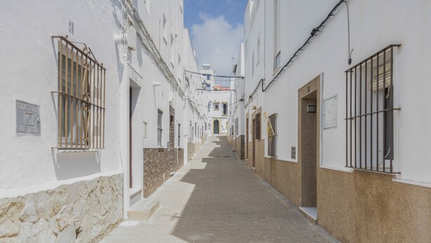 Una calle estrecha con edificios blancos, ventanas con rejas y cielo despejado.