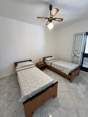 Een slaapkamer met twee bedden, een plafondventilator en een raam met jaloezieën.