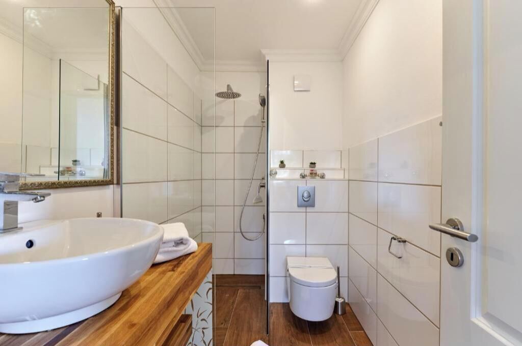 A modern bathroom with a large white sink, a wooden vanity, a glass shower enclosure, and a toilet.