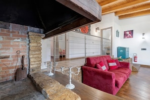 Una habitación con chimenea de ladrillo, sofá rojo y techo de madera.