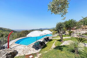 A swimming pool with a stone deck, outdoor umbrellas, and seating.