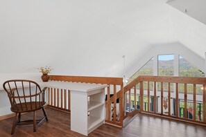A room with a wooden chair, a white desk, and a view of a balcony with a railing. - Cozy Murphy Cabin w/ Mountain Views (Murphy)