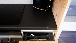 A kitchen with a black countertop, a wooden drawer with utensils, and a toaster on the counter. - C Gato 7 Riscas - Recanto Da Oliveira (Obidos)