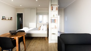 A modern, well-lit room with a bed, a dining table with chairs, a bookshelf, and a black armchair. - C Gato 7 Riscas - Recanto Da Oliveira (Obidos)