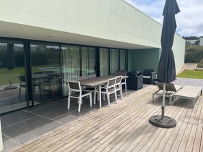 Une terrasse extérieure moderne, dotée d’une plateforme en bois, d’une table avec des chaises et d’un grand parasol.